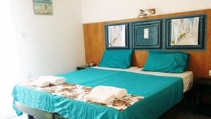 A bed with teal bedding, a wooden headboard, and two paintings above it. - Hotel Rea (Naxos)