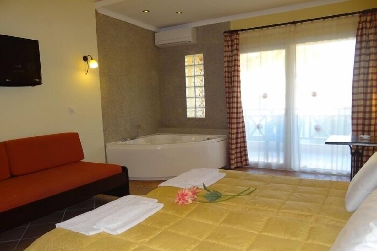Una habitación de hotel con una cama, un sofá rojo, una bañera y un balcón con cortinas.