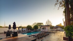 Ein Poolbereich mit Liegestühlen, einem kleinen Gebäude und einer Holzterrasse.