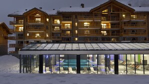 Eine mehrstöckige Holzhütte mit Balkonen und einem überdachten Poolbereich, Schnee auf dem Dach.
