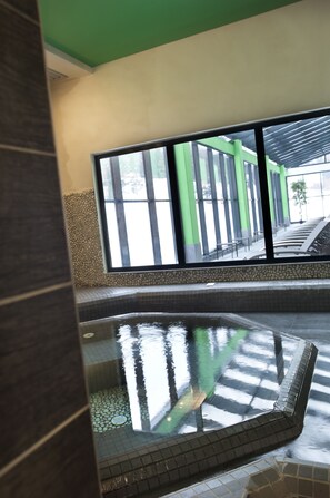 Un área de spa con suelo de baldosas, una pequeña piscina y vistas a un edificio con columnas verdes y un paseo techado.
