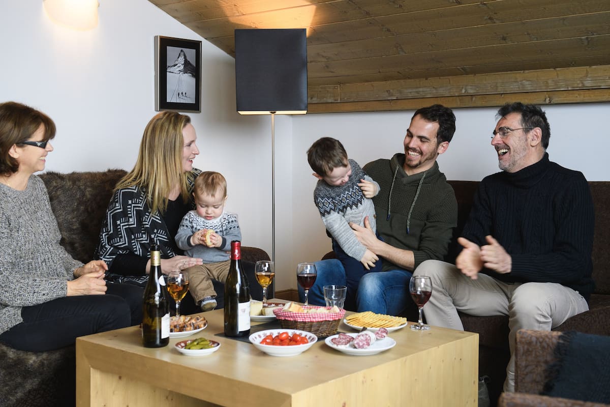 Eine Gruppe von Menschen sitzt auf einer Couch in einem gemütlichen Raum mit Holzbalkendecke und einem gerahmten Bild an der Wand.
