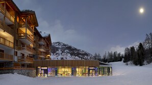 Ein mehrstöckiges Holzhaus mit Balkonen und einer Glasfassade, umgeben von Schnee und Bergen.