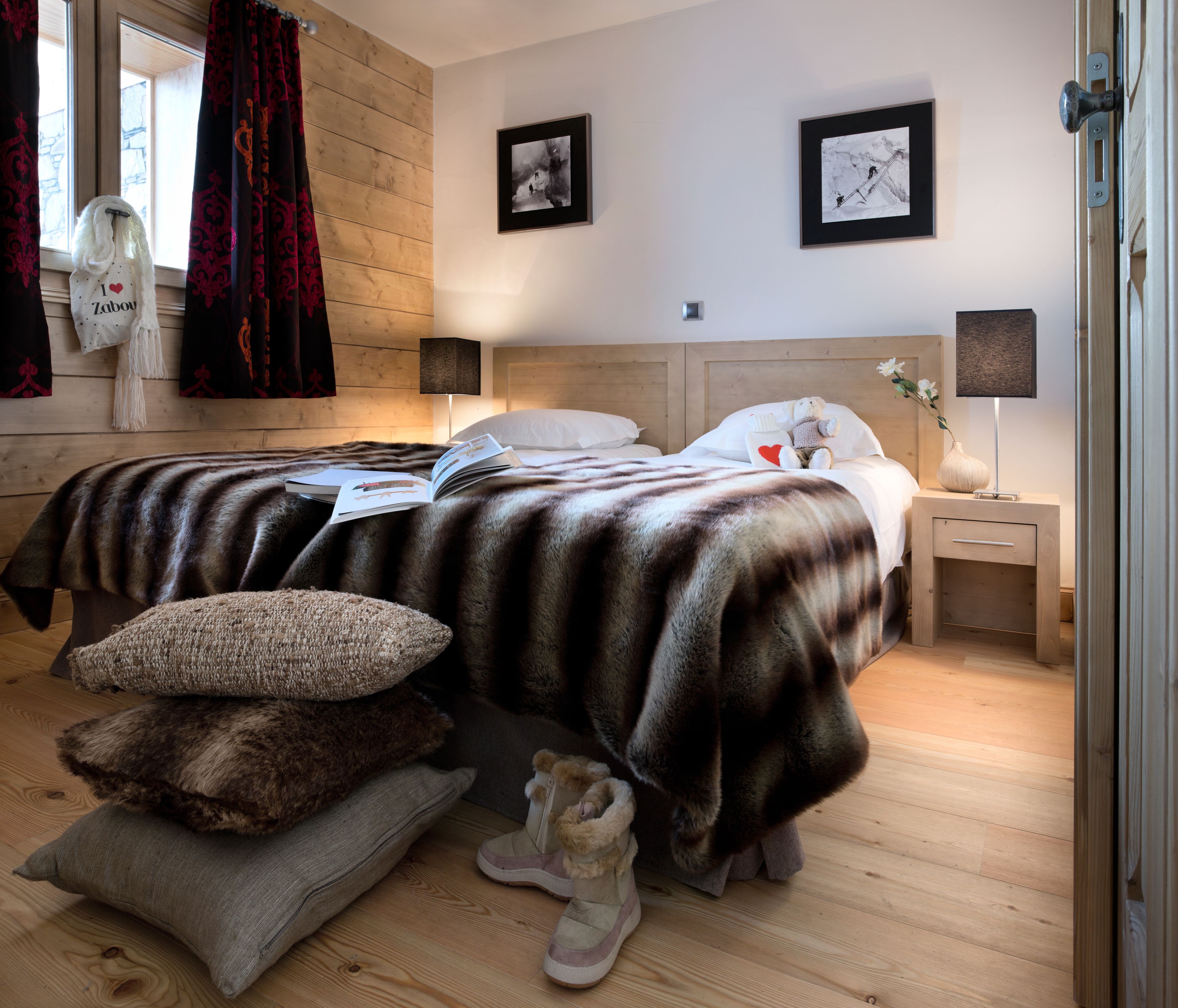 Un dormitorio con dos camas, cabeceros de madera, una mesita de noche con lámpara y una ventana con cortinas.