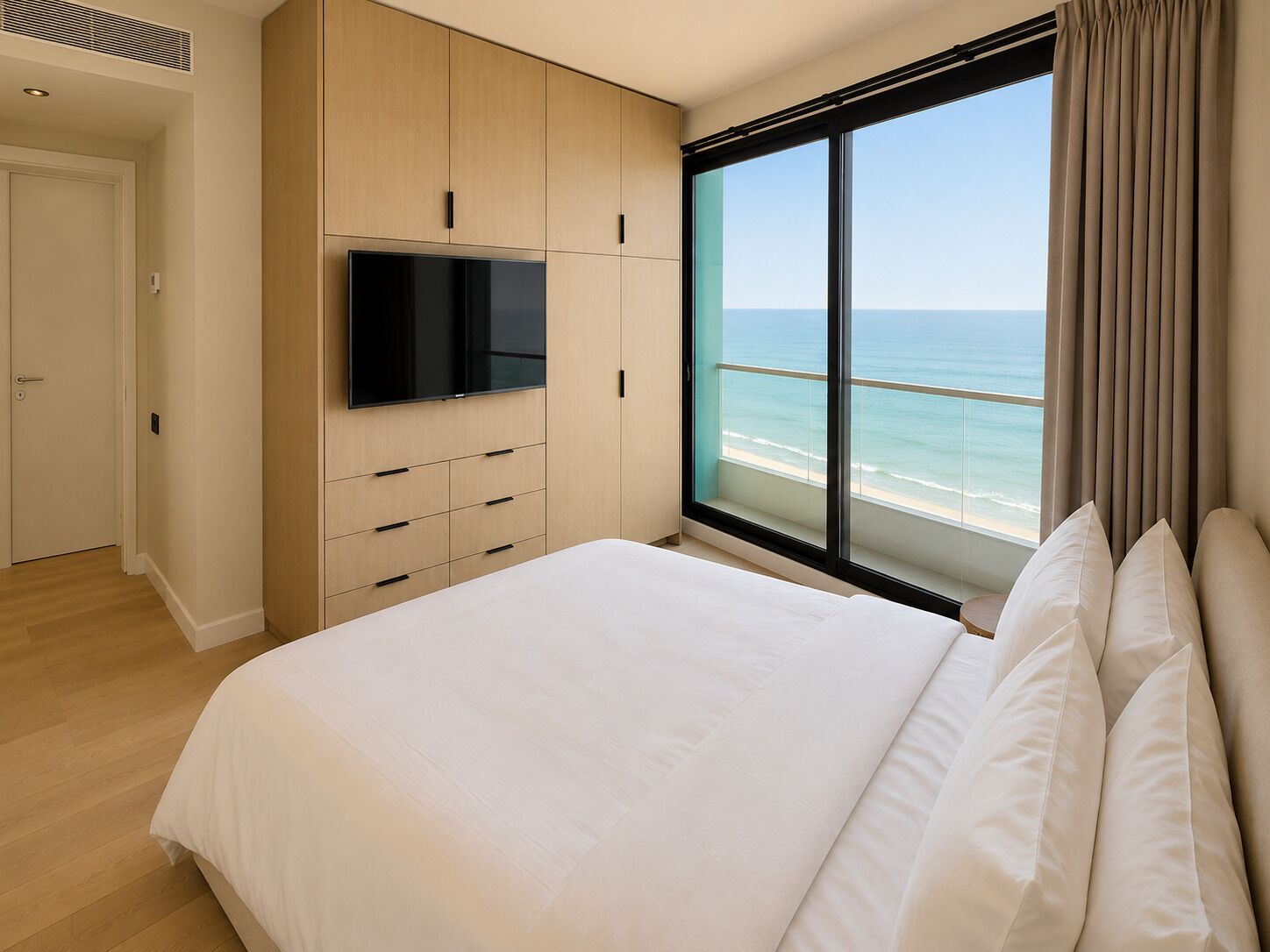 A bedroom with a large bed, a TV mounted on the wall, and a view of the ocean through a large window.