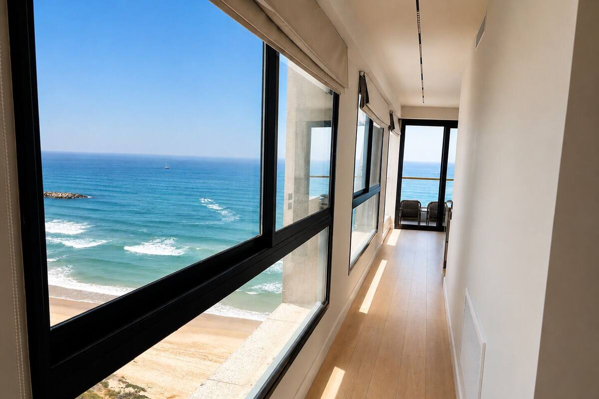 A corridor with large windows offering ocean views, a wooden floor, and a chair by the window.