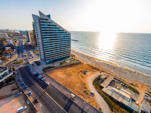 An aerial view of a coastal city with a prominent modern hotel, a beach, and a busy road.