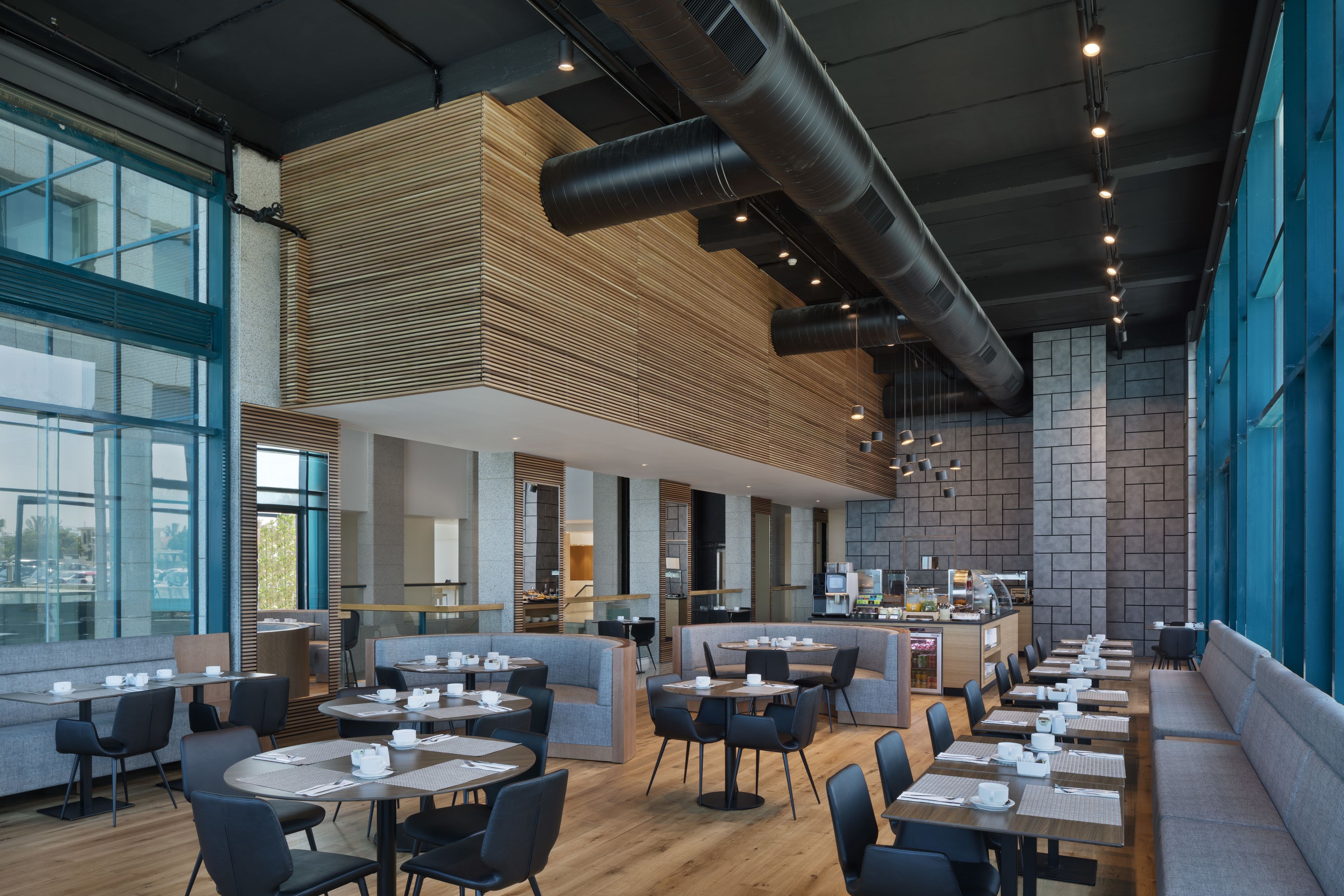 Een modern restaurant met hoge plafonds, zichtbaar ventilatiesysteem en een mix aan zitplaatsen, waaronder tafels en een aantal zitbanken.