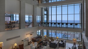 Un vestíbulo amplio con techo alto, ventanas grandes que ofrecen vista al mar y una zona de estar con muebles modernos.