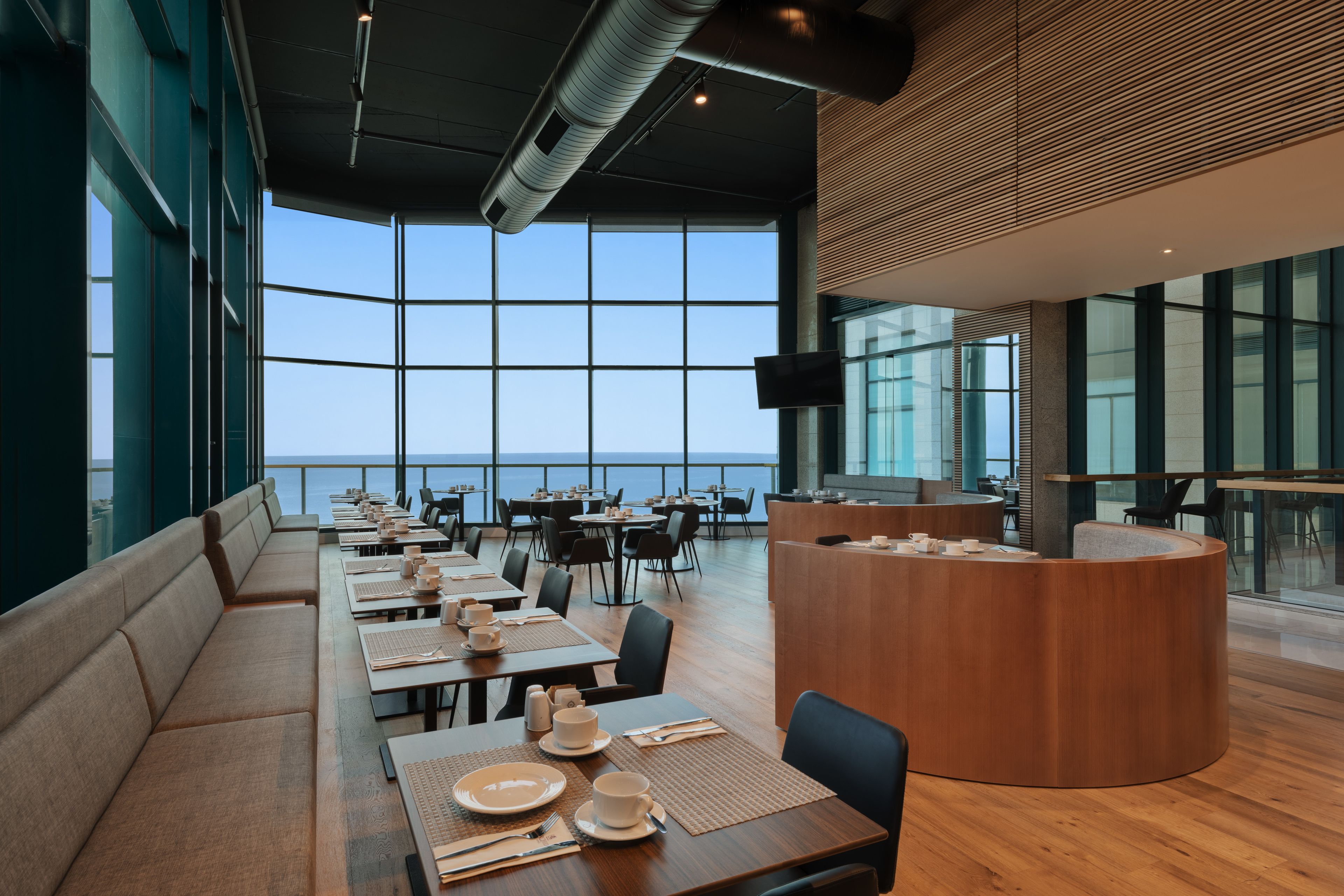 Un restaurante moderno con mesas largas, asientos acolchados y vista al mar.