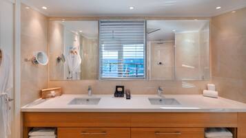 Un baño moderno con un espejo grande, dos lavamanos, armarios de madera y vistas al mar a través de la ventana.