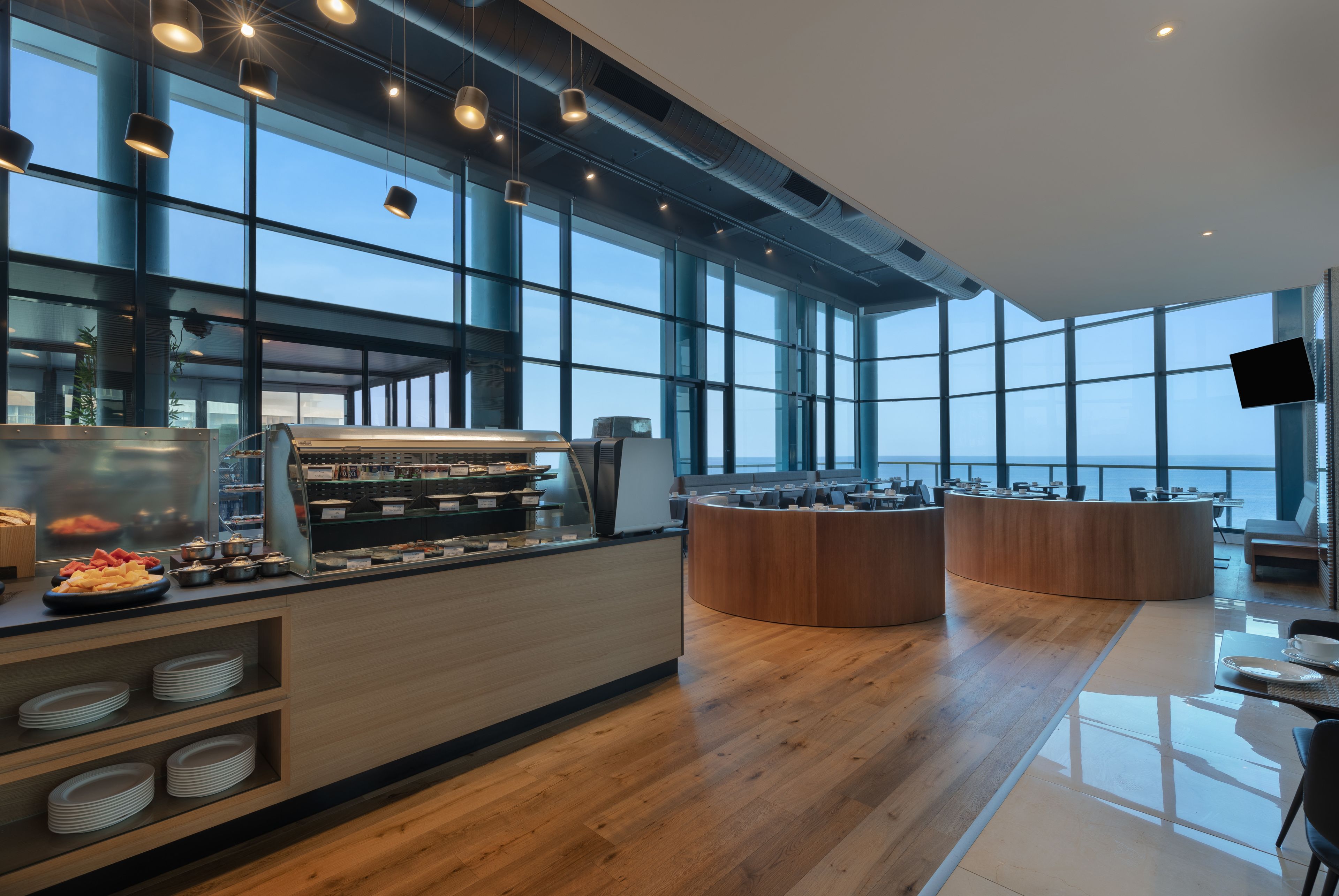 A modern cafe with a wooden counter, large windows, and a view of the sea.