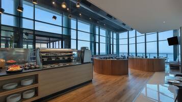 A modern cafe with a wooden counter, large windows, and a view of the sea.