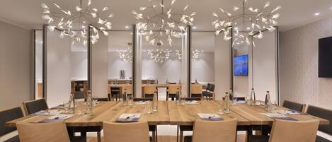A modern conference room with a long wooden table, multiple chairs, and a unique chandelier.