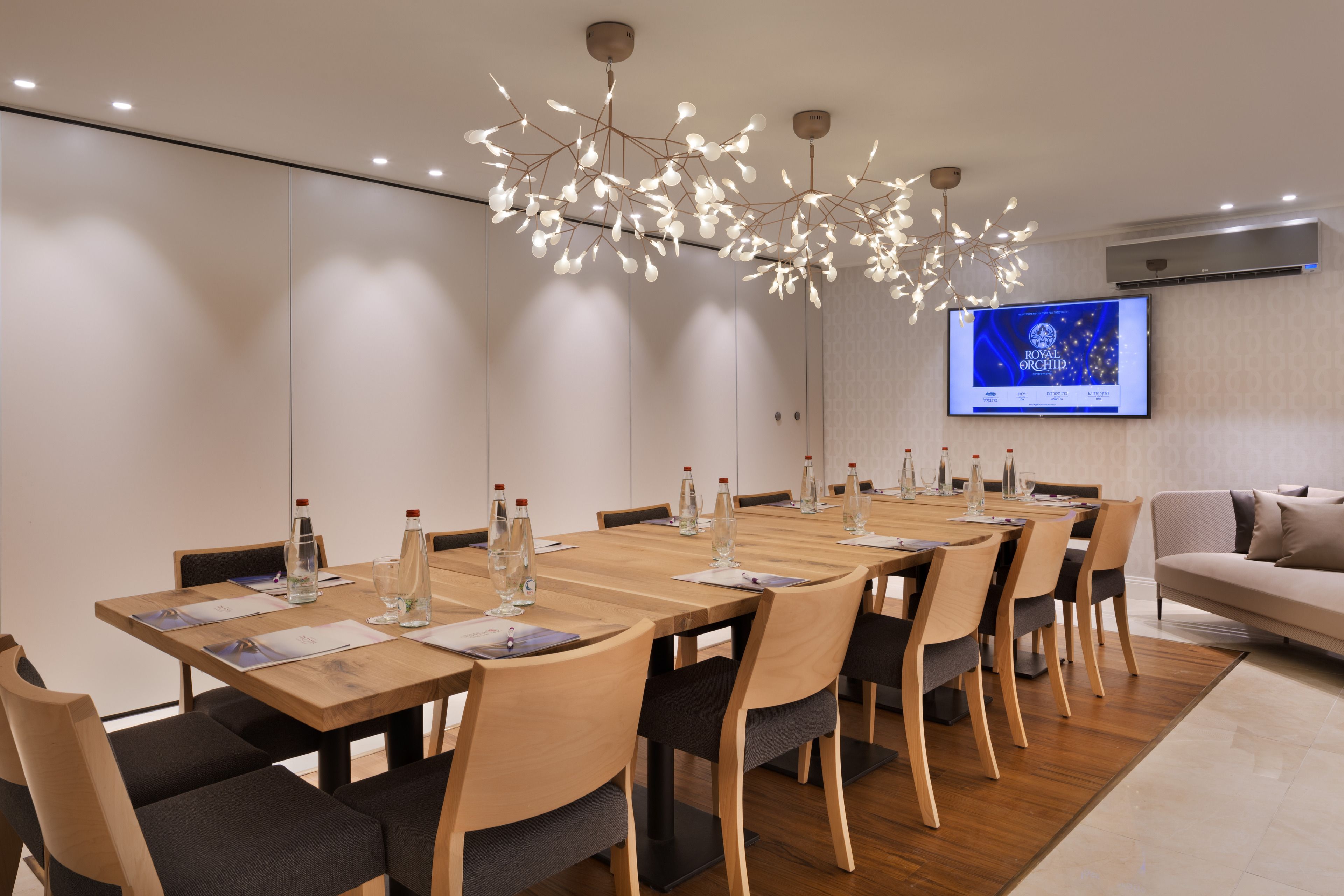 A modern dining area with a long wooden table, multiple chairs, and a unique chandelier.