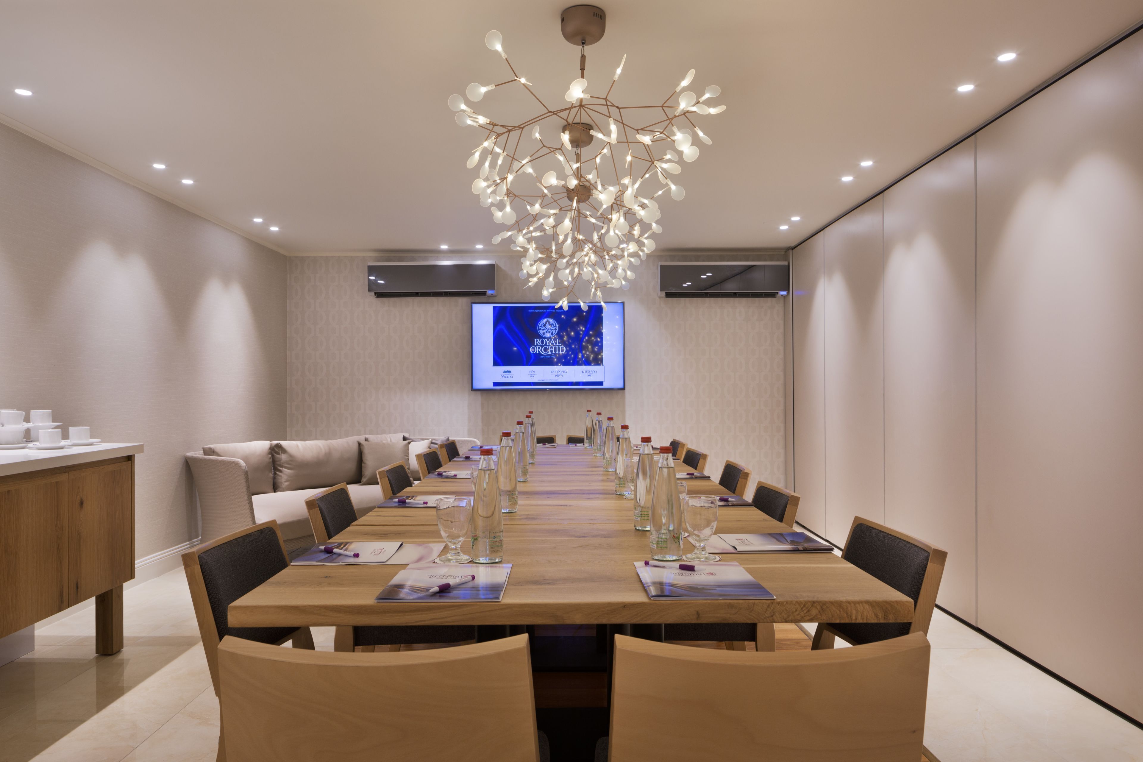 Un salón de conferencias con una larga mesa, sillas, una araña de cristal, una pantalla de televisión y una estación de café.