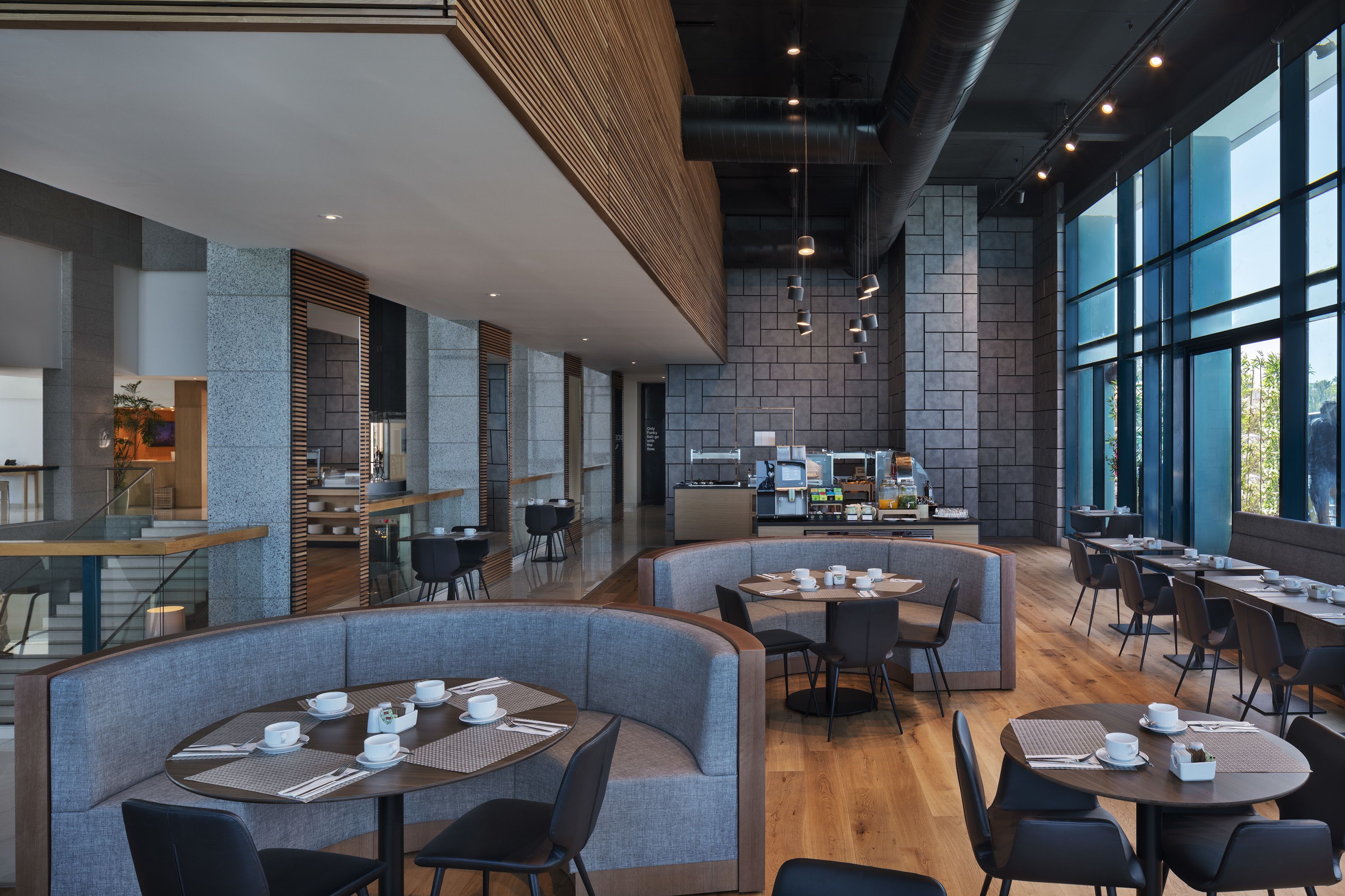 A modern restaurant with high tables and booths, a kitchen area, and large windows.