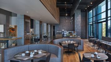 A modern restaurant with high tables and booths, a kitchen area, and large windows.