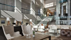 Un lobby espacioso con techo alto, mobiliario moderno y una escalera que conduce a plantas superiores.