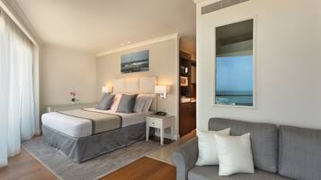 Une chambre d’hôtel moderne, dotée d’un grand lit, d’un canapé, d’une petite table et d’un tableau représentant un paysage côtier.