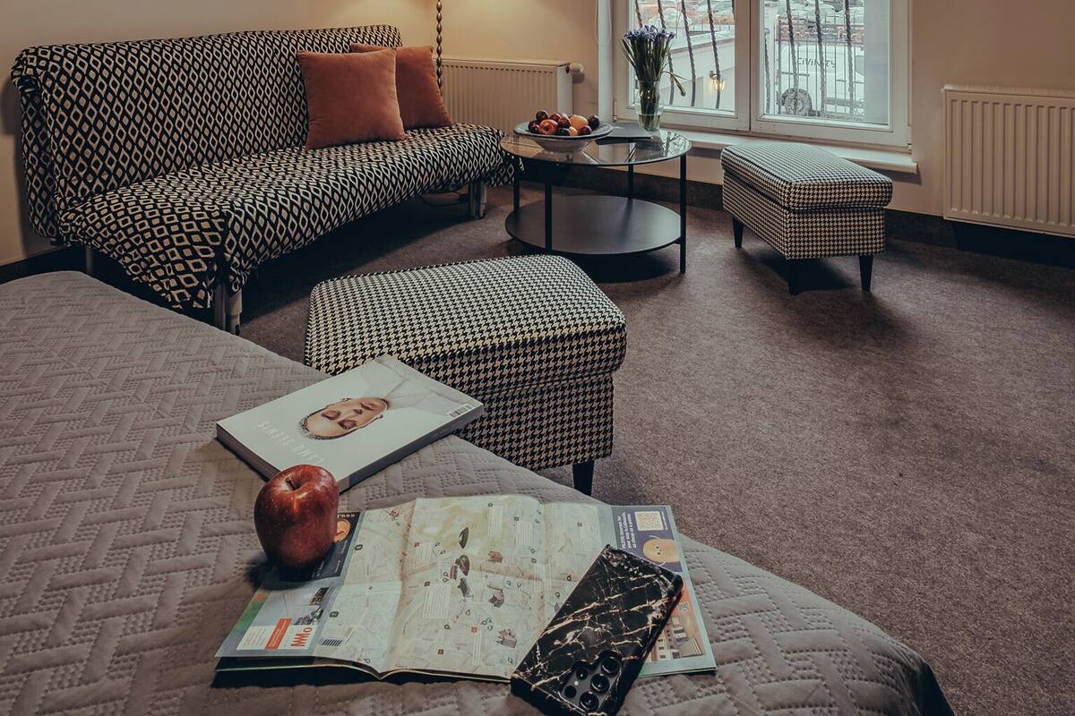 Een gezellige kamer met een gestreept sofa, een ronde salontafel, een leeshoek met een boek en appel, en een raam met uitzicht.