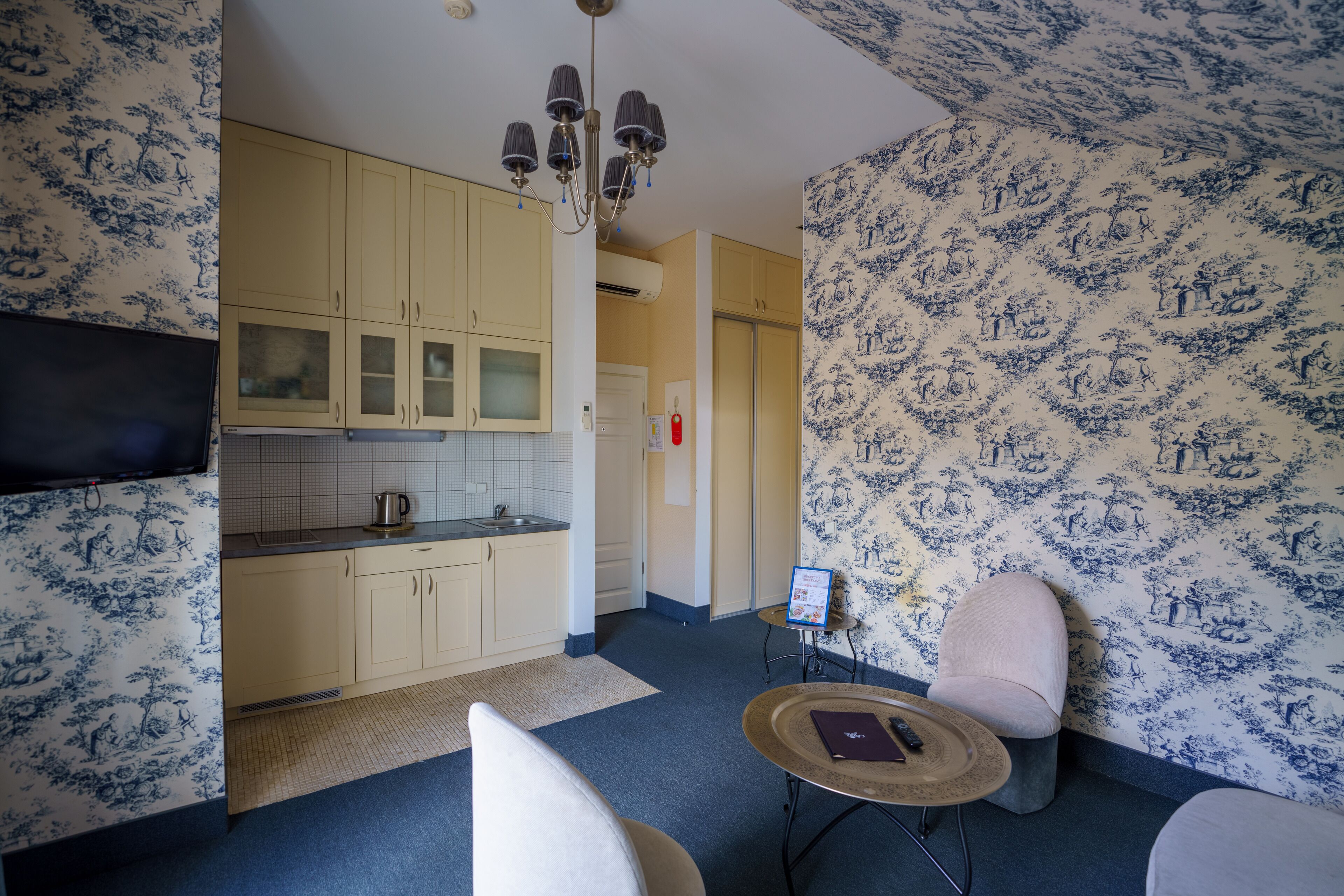 Una habitación con cocina, comedor con mesa y sillas, y una pared con diseño azul y blanco.