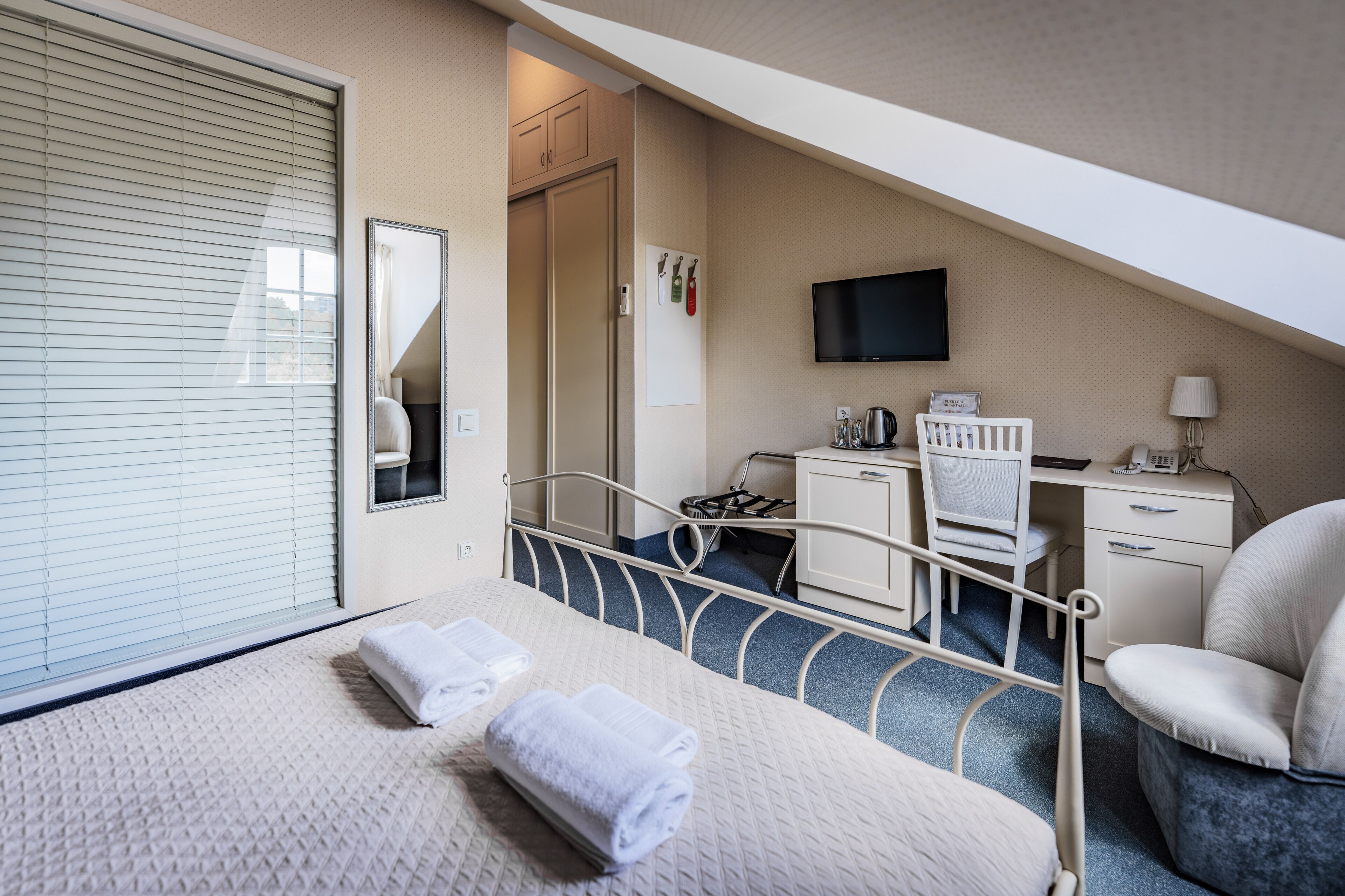 A hotel room with a bed, a desk, a chair, a television, and a window with blinds.