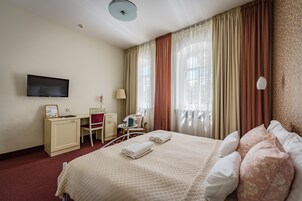 Habitación de hotel con cama, escritorio, silla, televisor y cortinas.