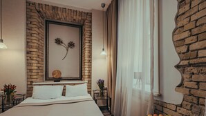 A modern bedroom with a brick accent wall, a large bed with white linens, a bedside table with a fruit bowl, and a wall-mounted mirror.