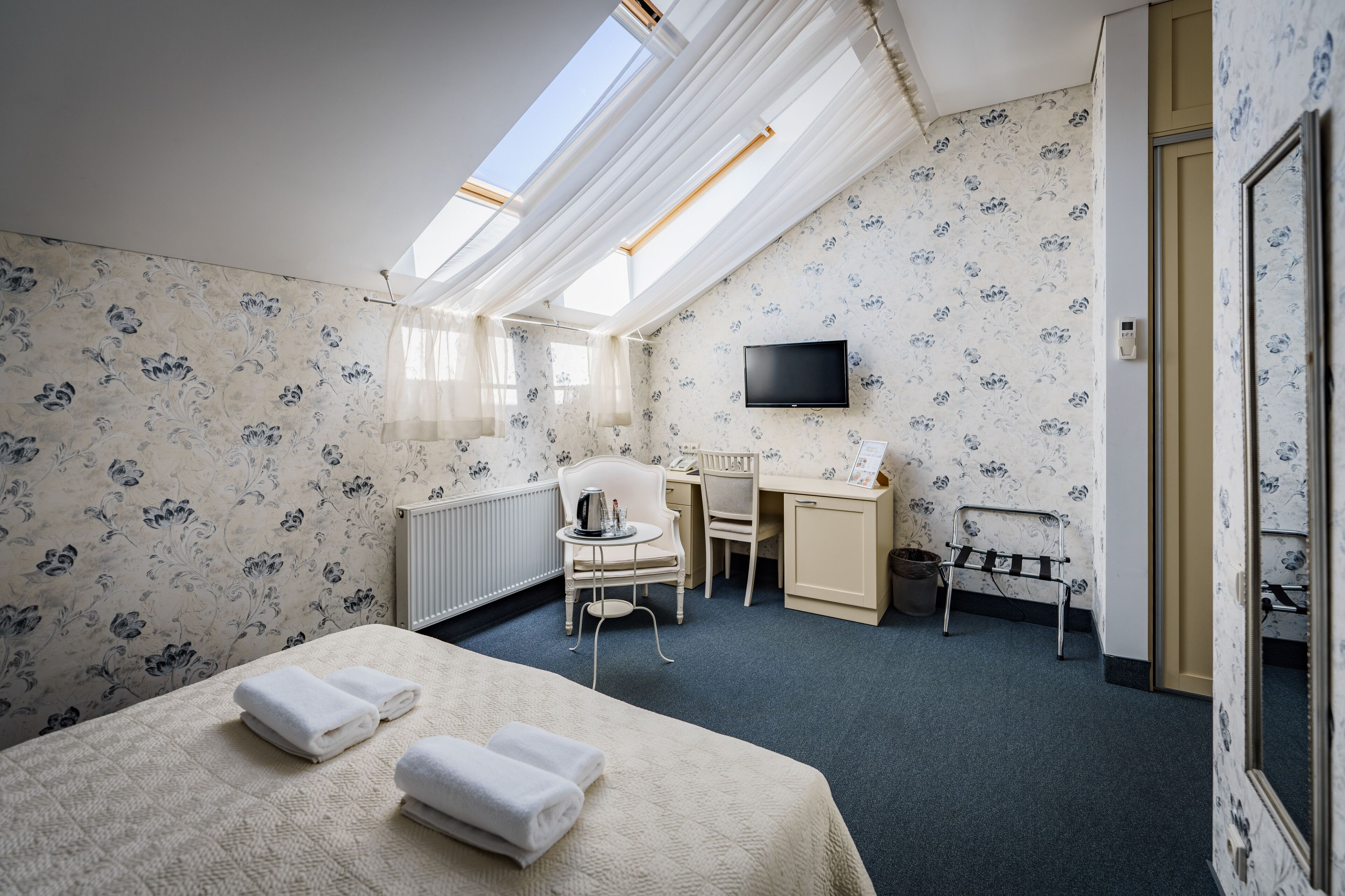 Habitación de hotel con cama, escritorio, silla, televisor y ventana con cortinas.