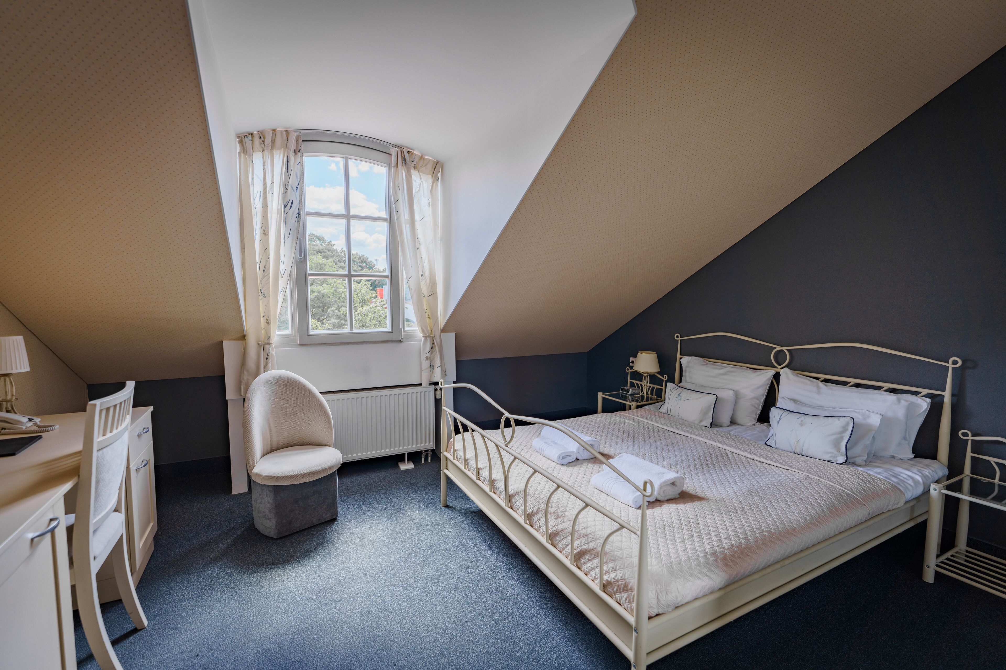 A bedroom with a bed, a desk, a chair, a window, and a radiator.