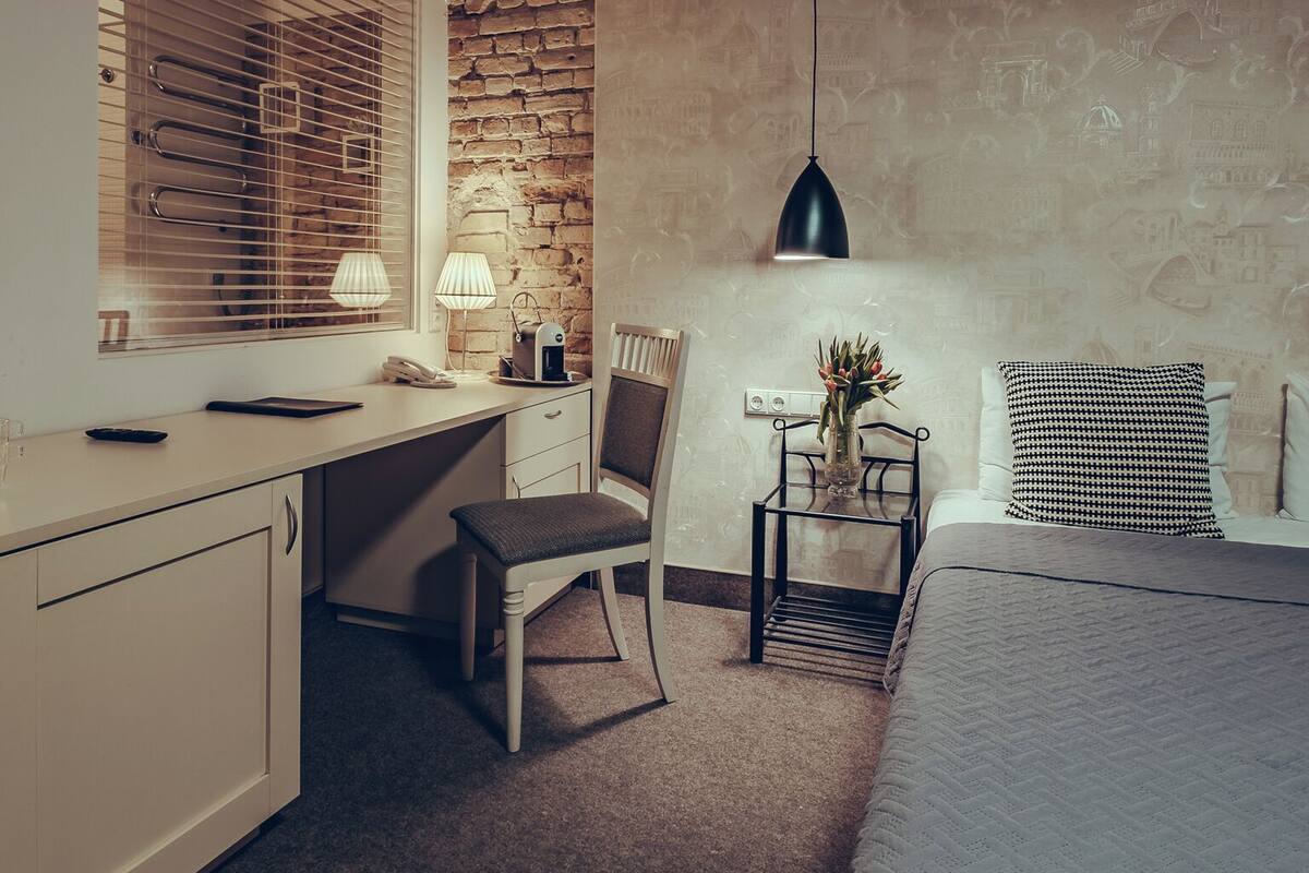 Een moderne slaapkamer met een bed, een bureau en een stoel. Er staat een lamp op het bureau en een vaas met bloemen op het nachtkastje.