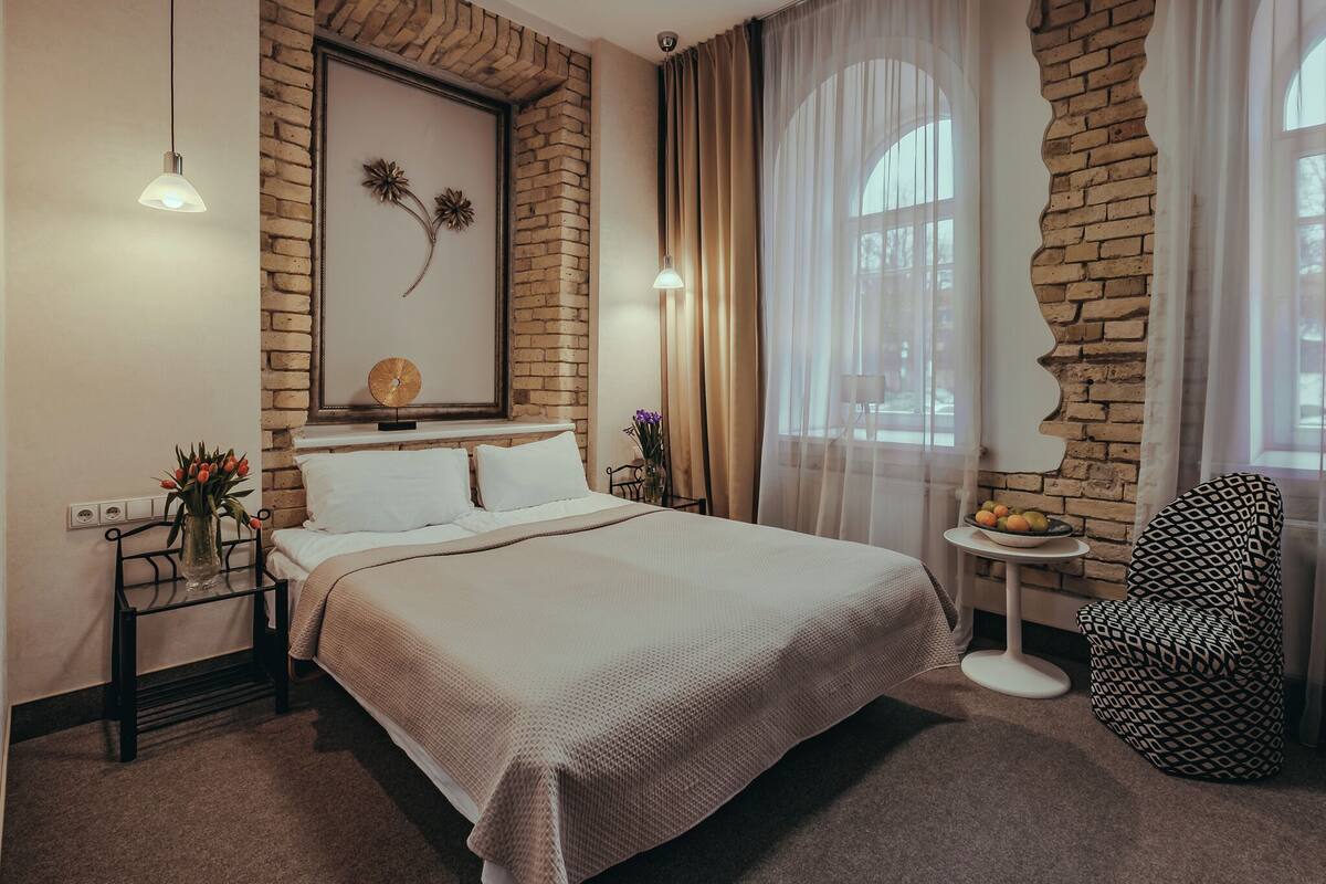 Een keurig opgemaakt hotelkamer met een bed, een klein tafeltje met fruit en een gestreept fauteuil.