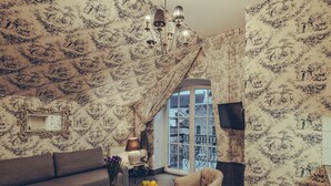 A living room with patterned wallpaper, a sofa, a coffee table with fruit, a lamp, and a chair.