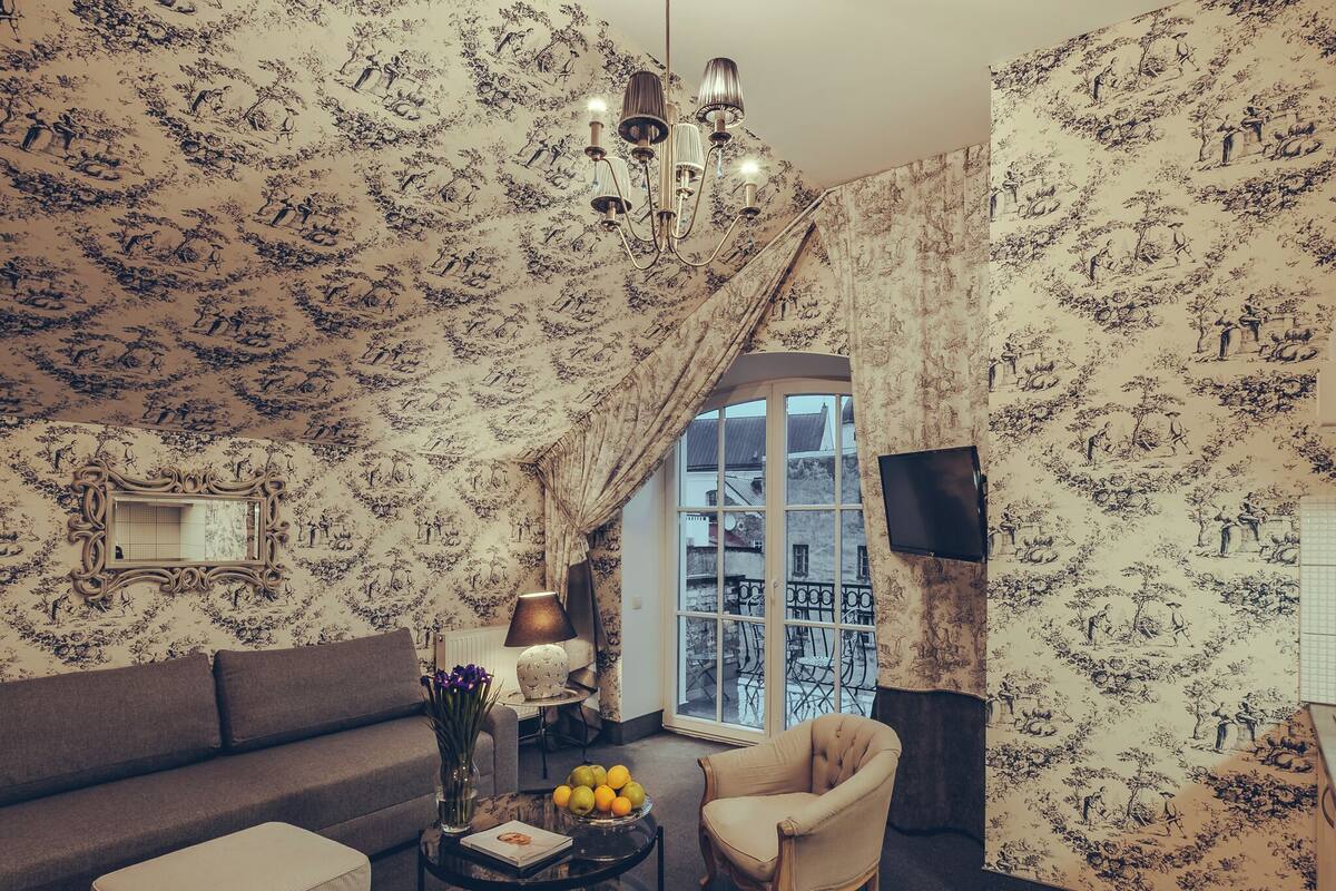 Een woonkamer met behang met patroon, een bank, een salontafel met fruit, een lamp en een stoel.