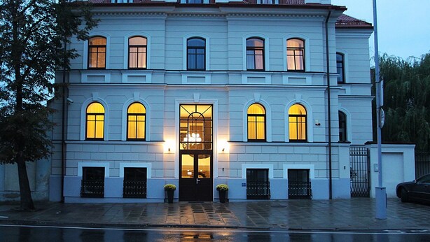A two-story building with a symmetrical facade, arched windows, and a central entrance with a glass door.