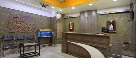 A reception area with a wooden reception desk, a wall-mounted sculpture, and a ceiling fan.