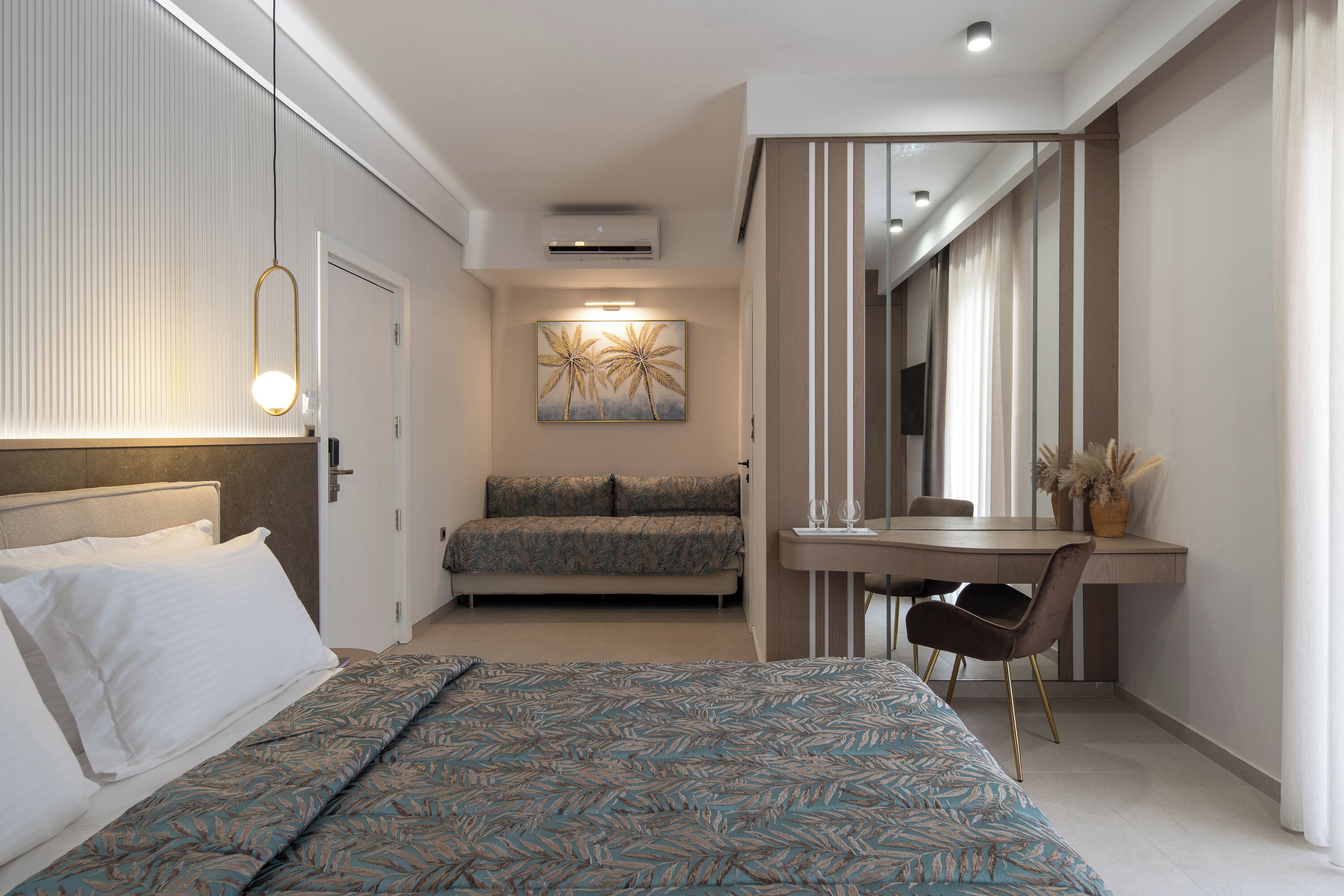 A modern hotel room with a large bed, a sofa, a desk with a chair, and a mirror.