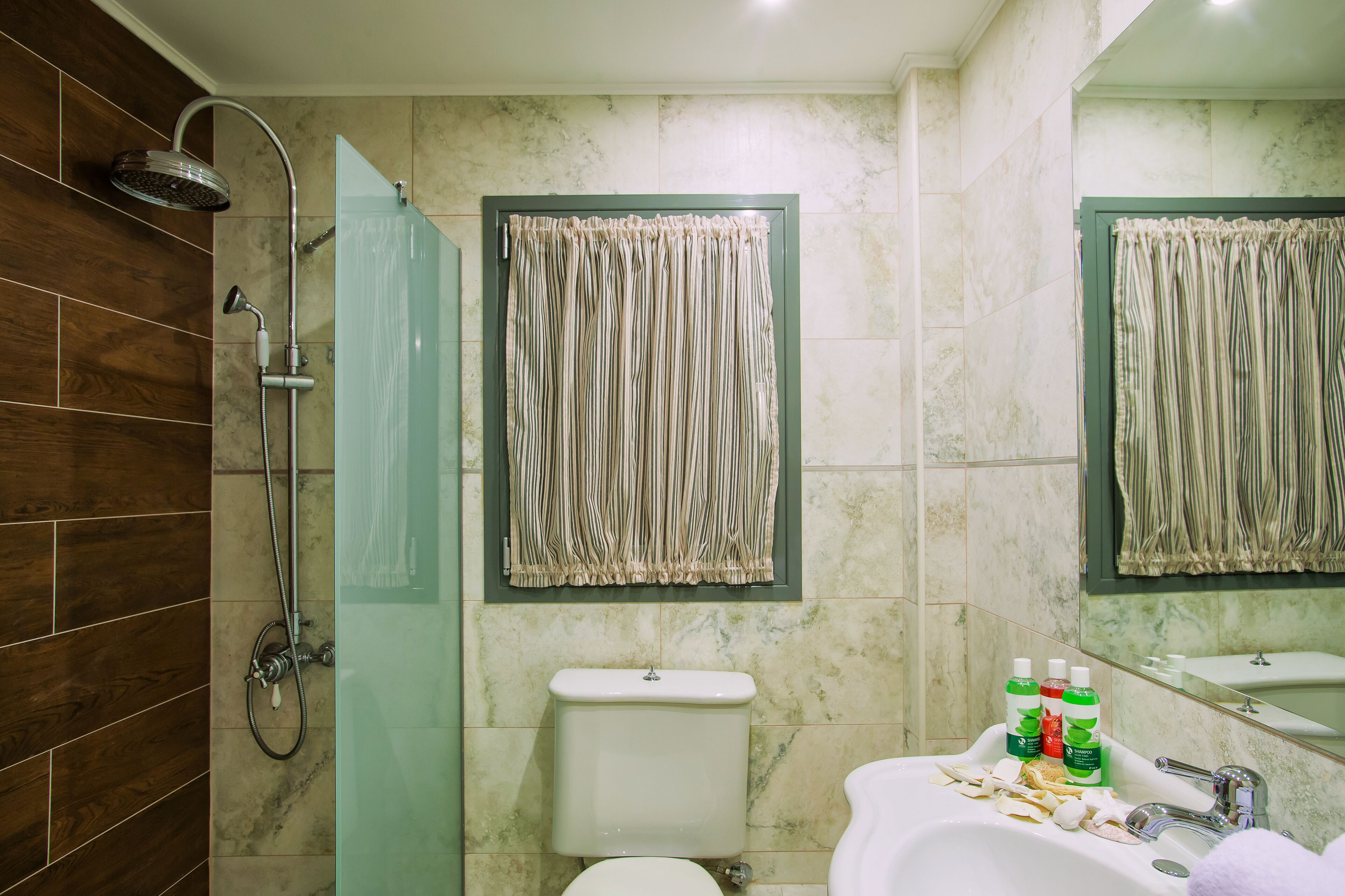 A bathroom with a shower, toilet, sink, and a mirror.