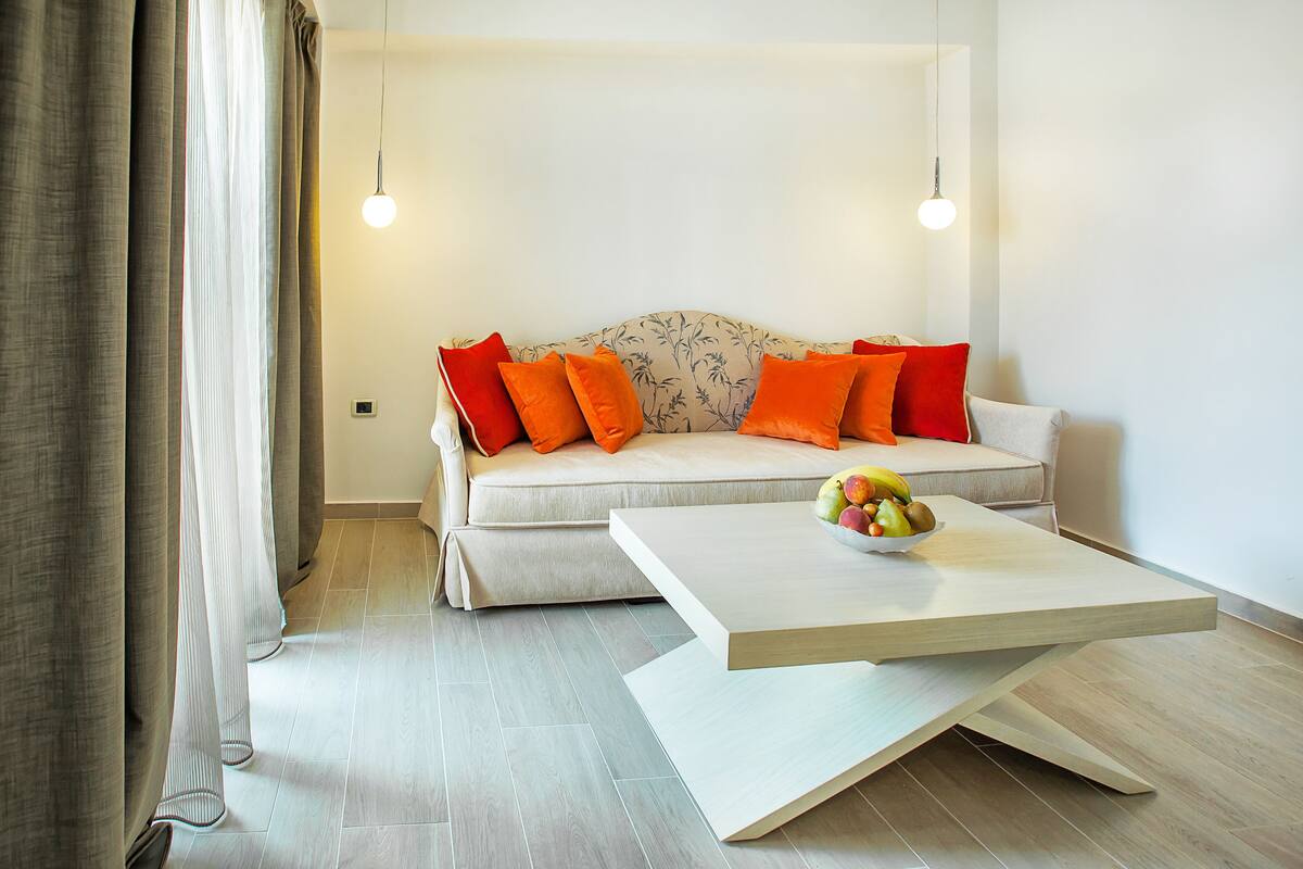A modern living room with a sofa, orange cushions, a coffee table with fruit, and hanging pendant lights.