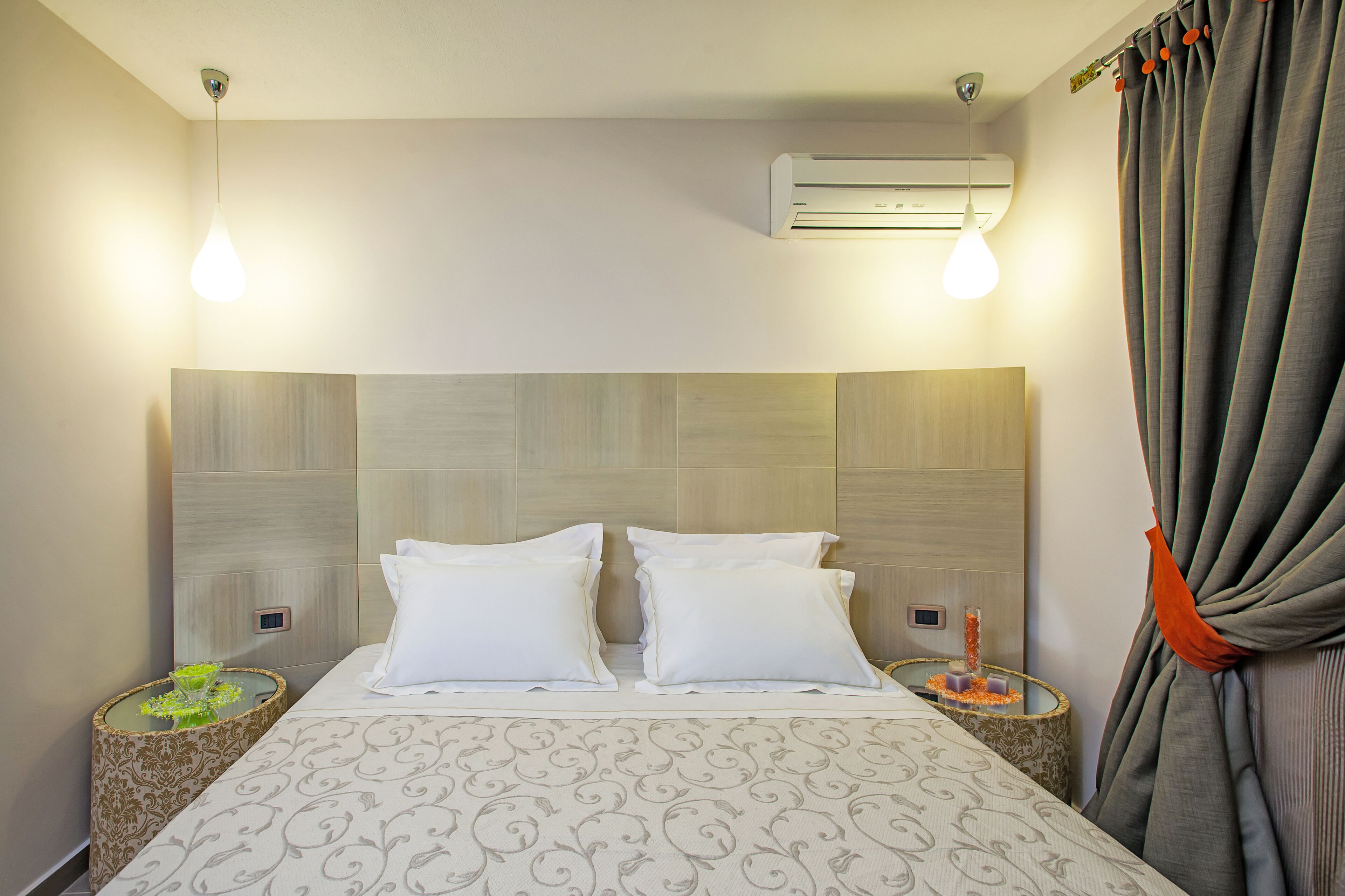 Una habitación de hotel con una cama, dos mesitas de noche, un aire acondicionado y una cortina.