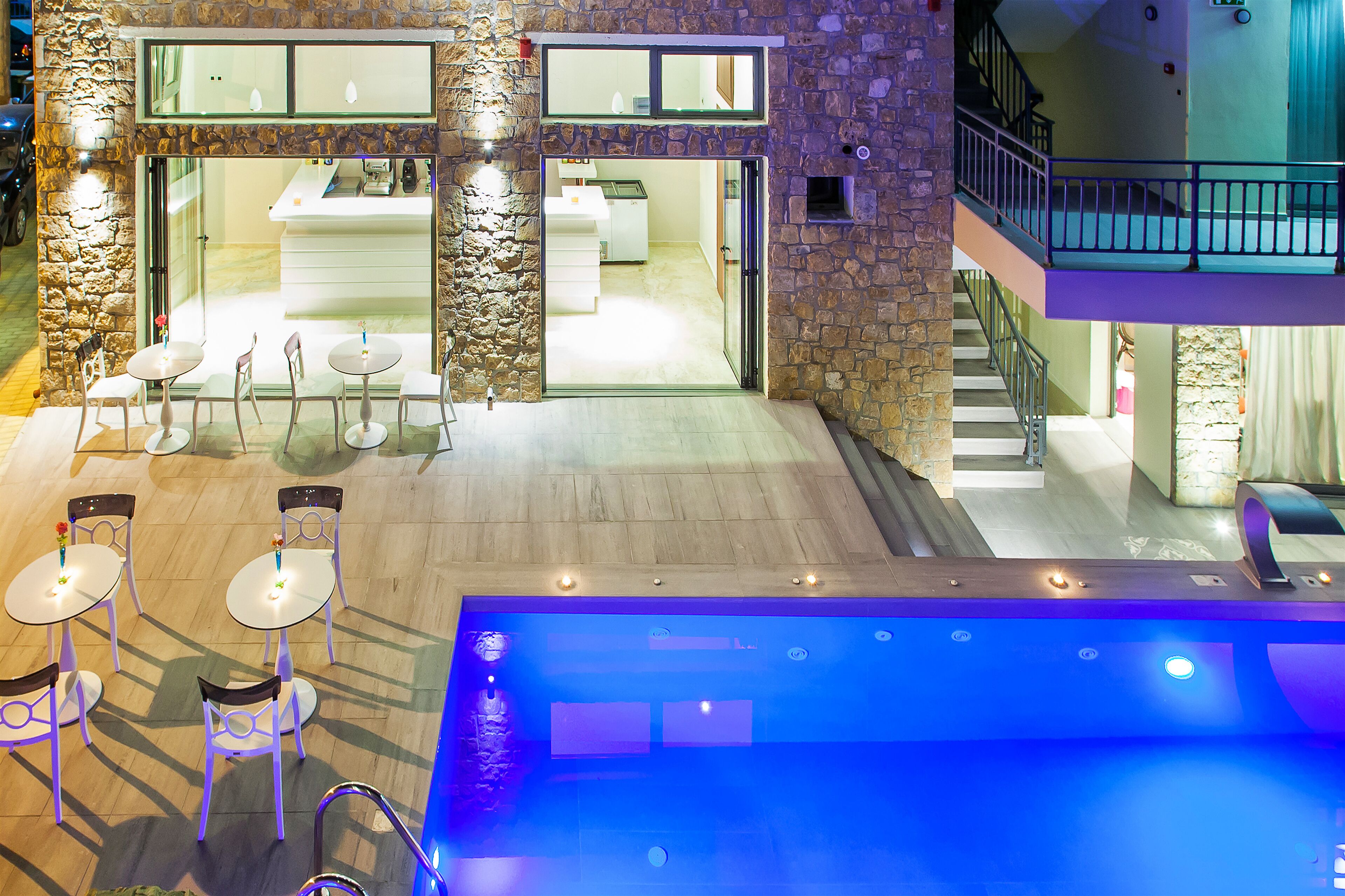 An indoor swimming pool area with a stone wall, multiple seating tables, and a staircase leading to an upper level.