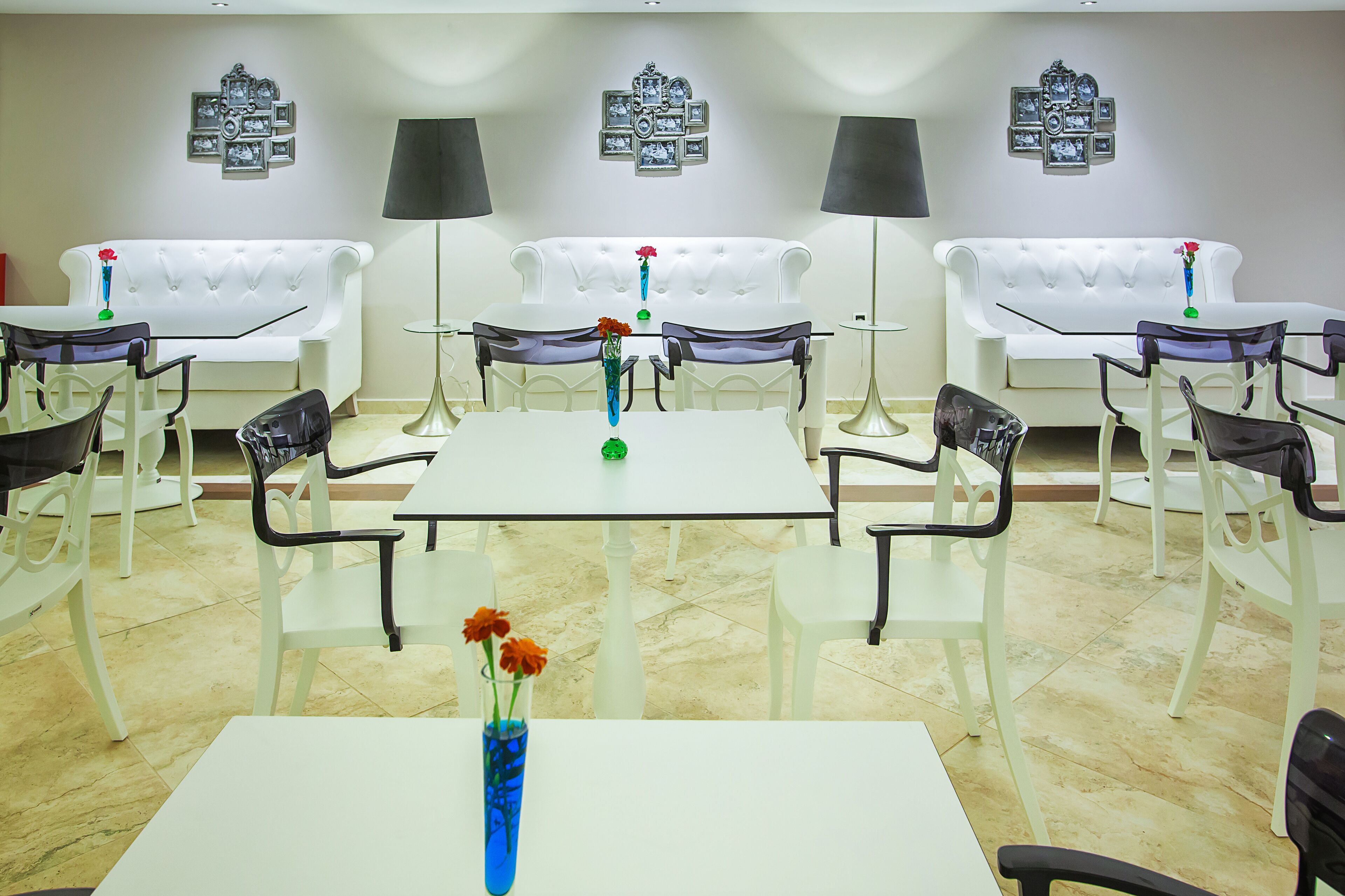 A hotel room with a white sofa set, a dining table with chairs, and a wall adorned with framed photographs.