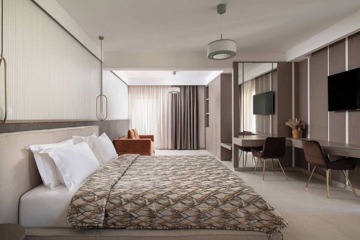 A modern hotel room with a large bed, a desk, and a TV.