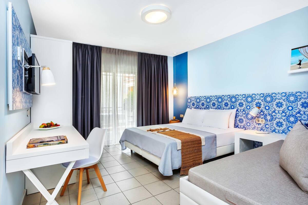 A hotel room with a bed, a desk, a chair, and a sofa.