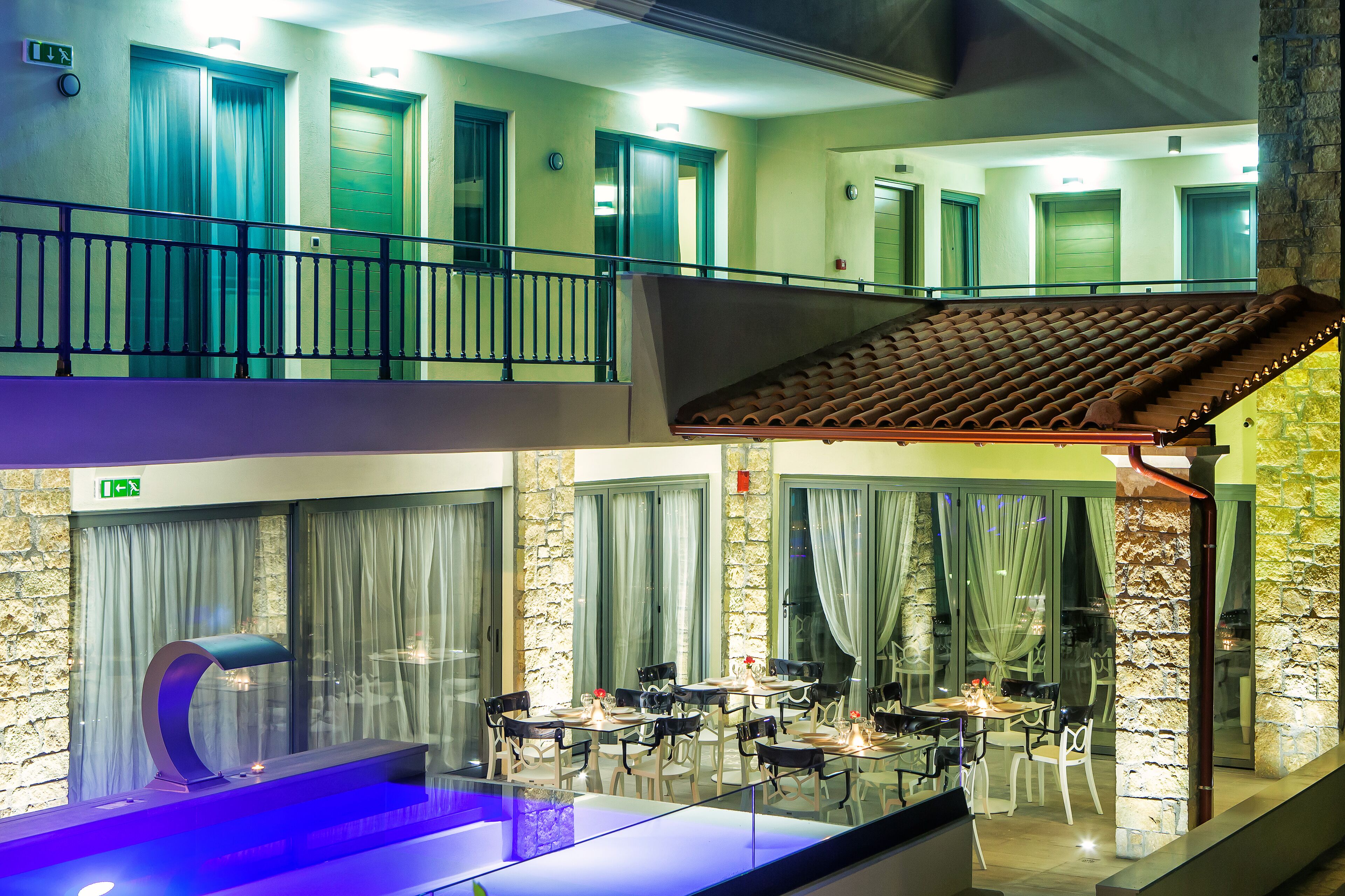 A hotel lobby with a glass-enclosed pool, a dining area with tables and chairs, and a staircase leading to an upper floor.