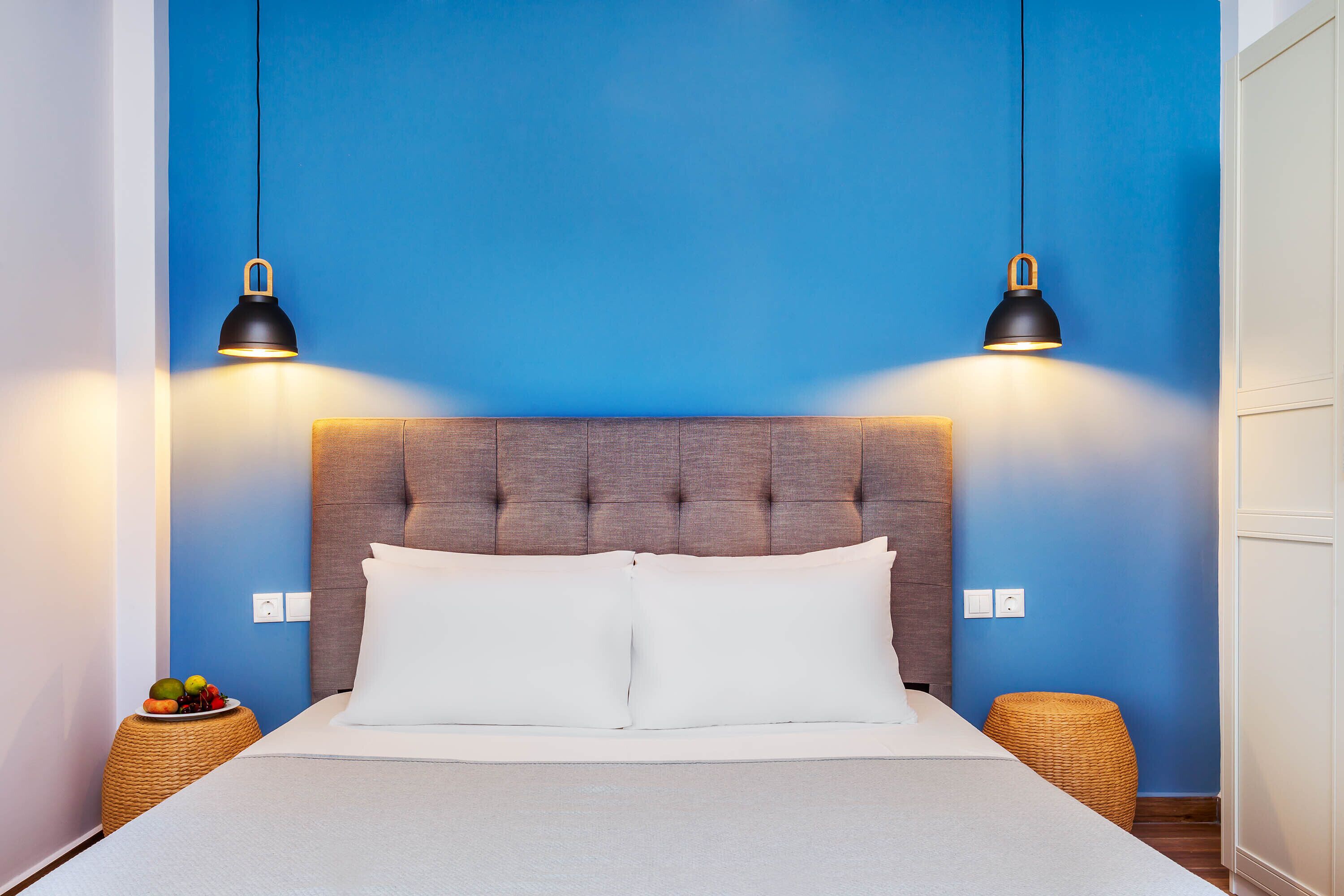 A neatly made bed with white linens, a tufted headboard, and two black pendant lights.