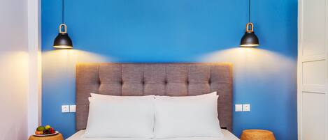 A neatly made bed with white linens, a tufted headboard, and two black pendant lights.