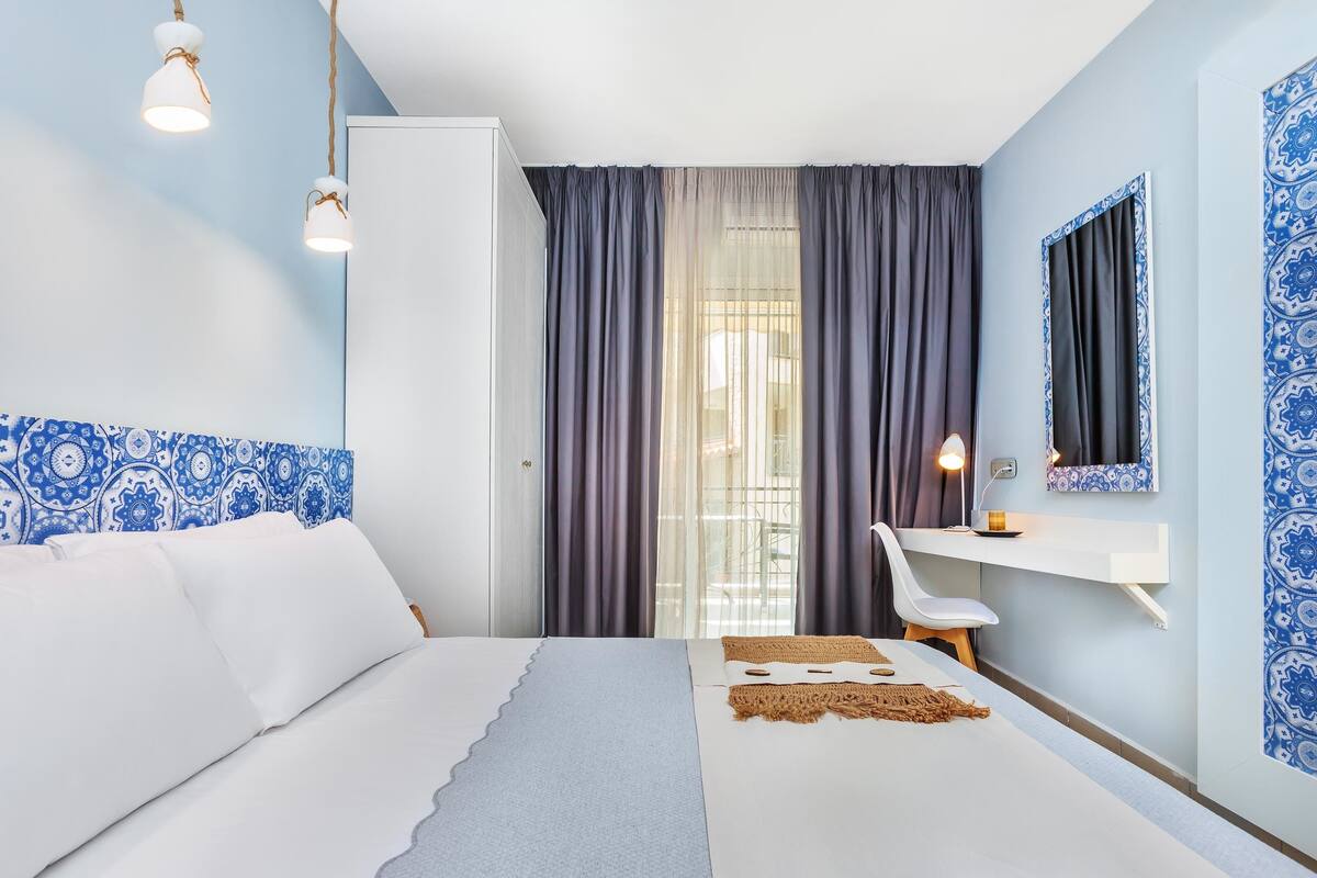 A modern bedroom with a bed, bedside table, chair, and a large window with curtains.
