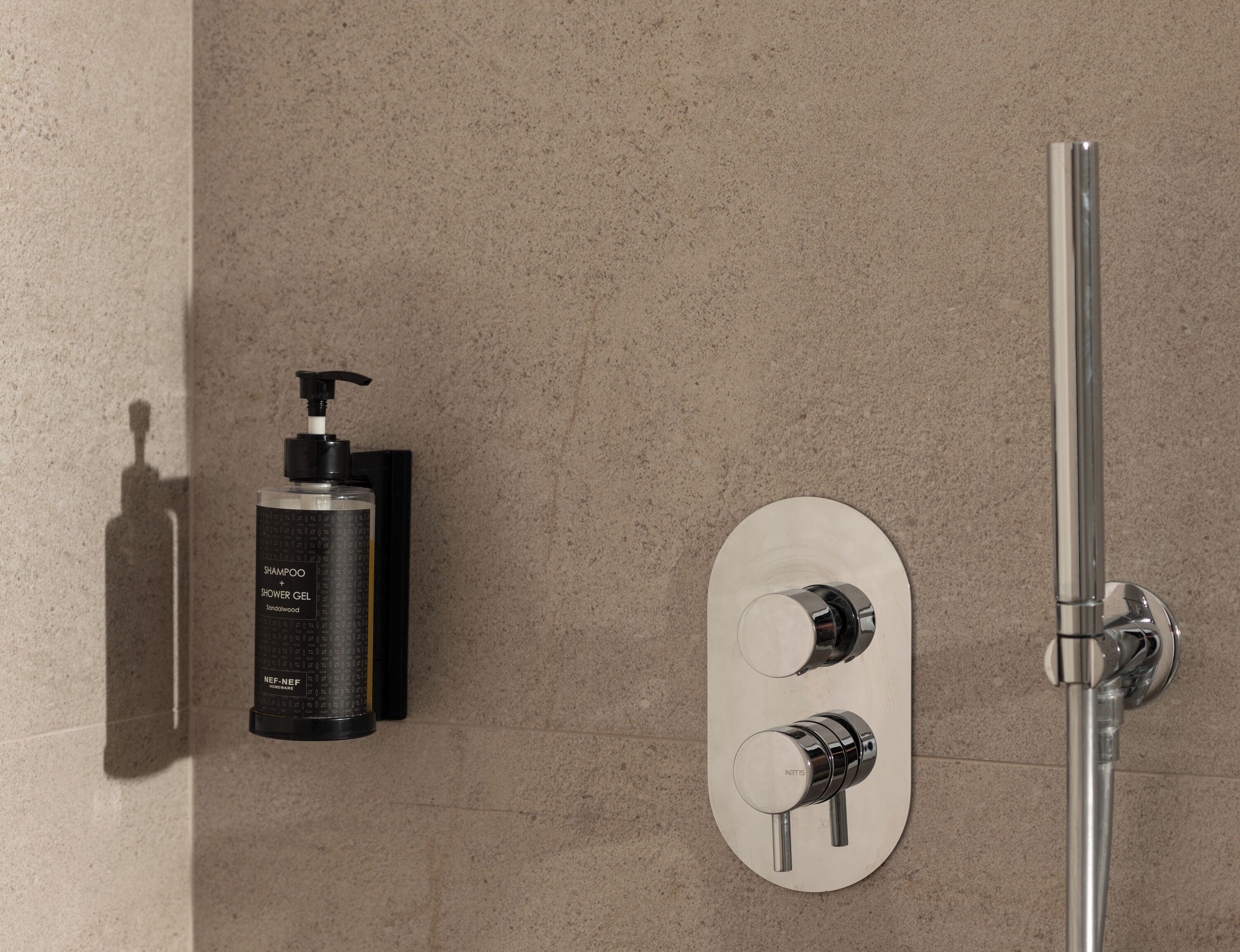 Une salle de bain avec une douche, un pommeau de douche amovible, et une bouteille de shampoing et de gel douche.